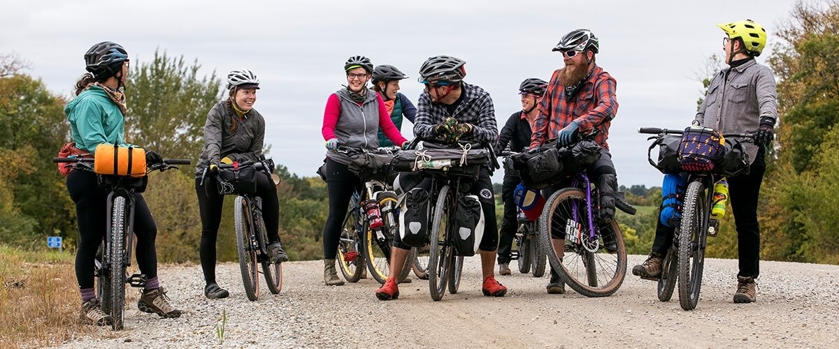 A group of cyclists stand together over their bikes, laughing and smiling.