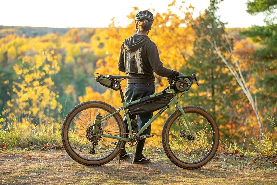 Cyclist stands with his bike loaded with gear overlooking yellow aspen trees. 