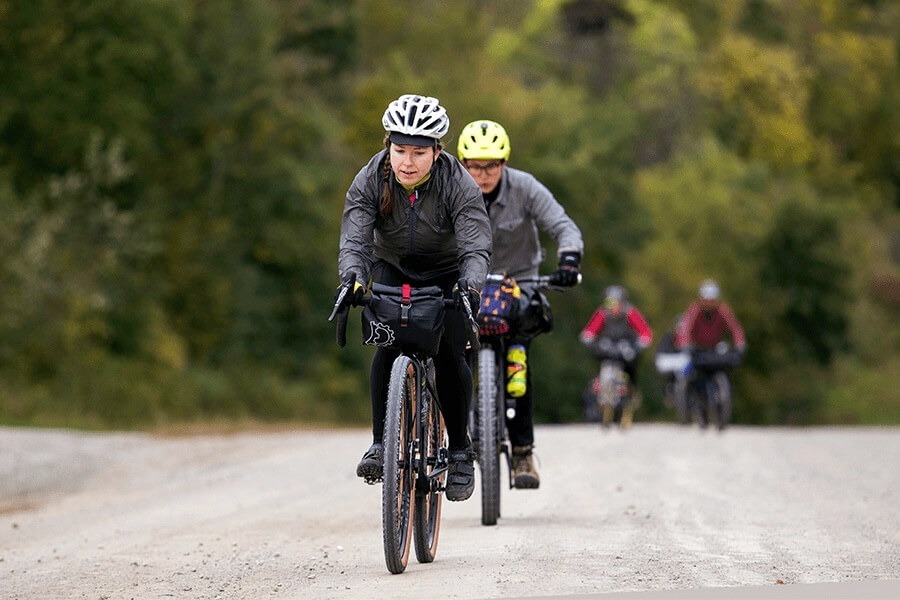 Bikepacking cyclists ride together on a gravel road lined with trees.