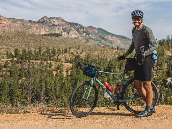 Jalen Bazile standing with his gravel bike in front of tree-lined mountain range