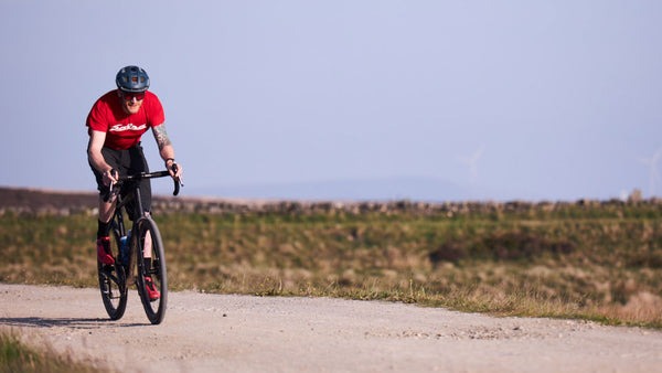Steve Bate rides his drop bar bike on a gravel road while wearing a red t-shirt