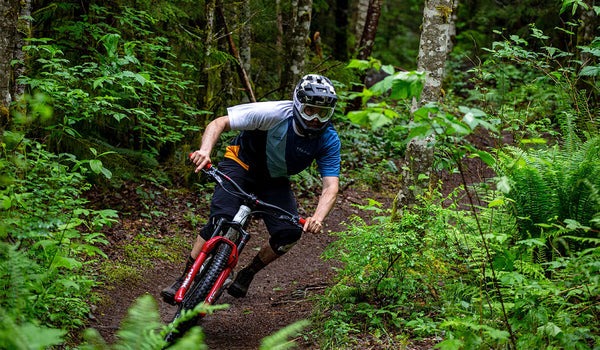 A cyclist on a forested mountain bike trail rounds a corner.