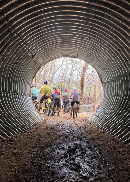 Collage of two images. On the left a group of riders are shown at the end of tunnel on mountain bikes. On the right clipboards and sharpie markers for taking notes.