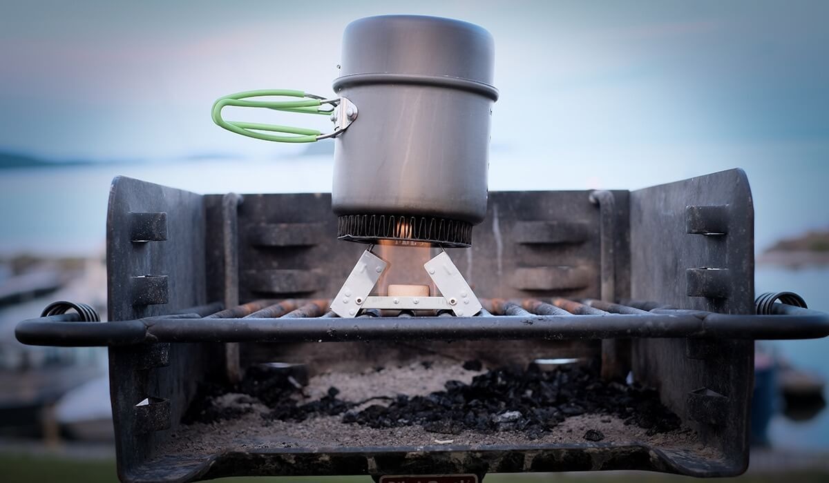 A small camp stove is sitting on top of the grates of a park grill