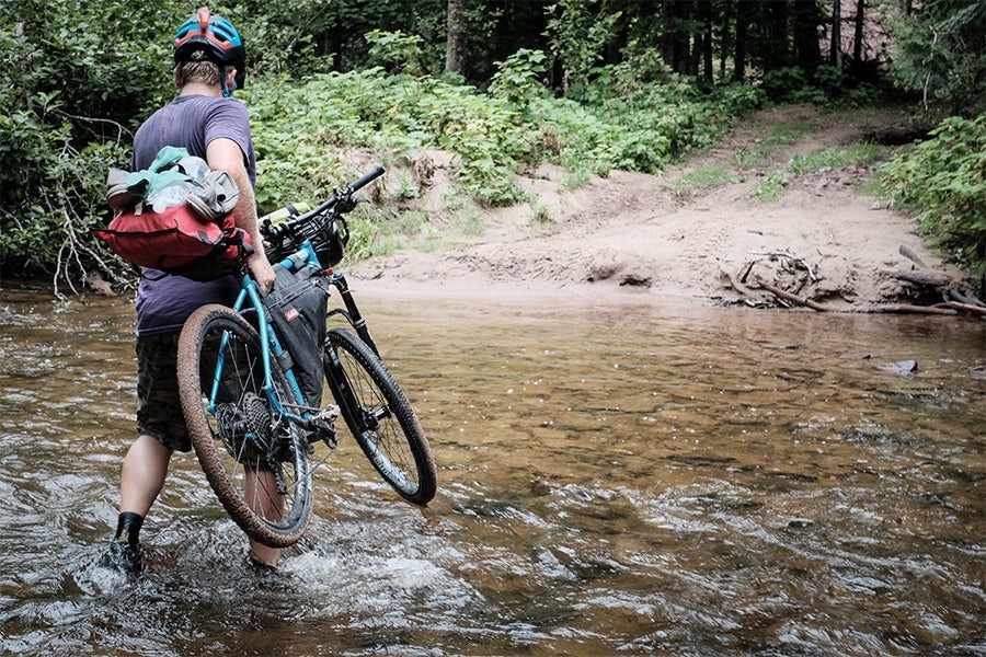A cyclist carries his bike loaded with gear over a water crossing