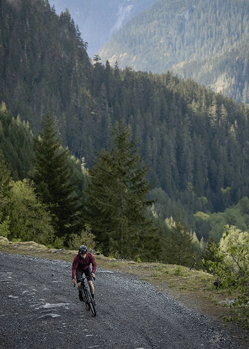 2 images. Left is a sprawling green valley beside a mountain. Right is Chris riding a gravel road in the mountains.