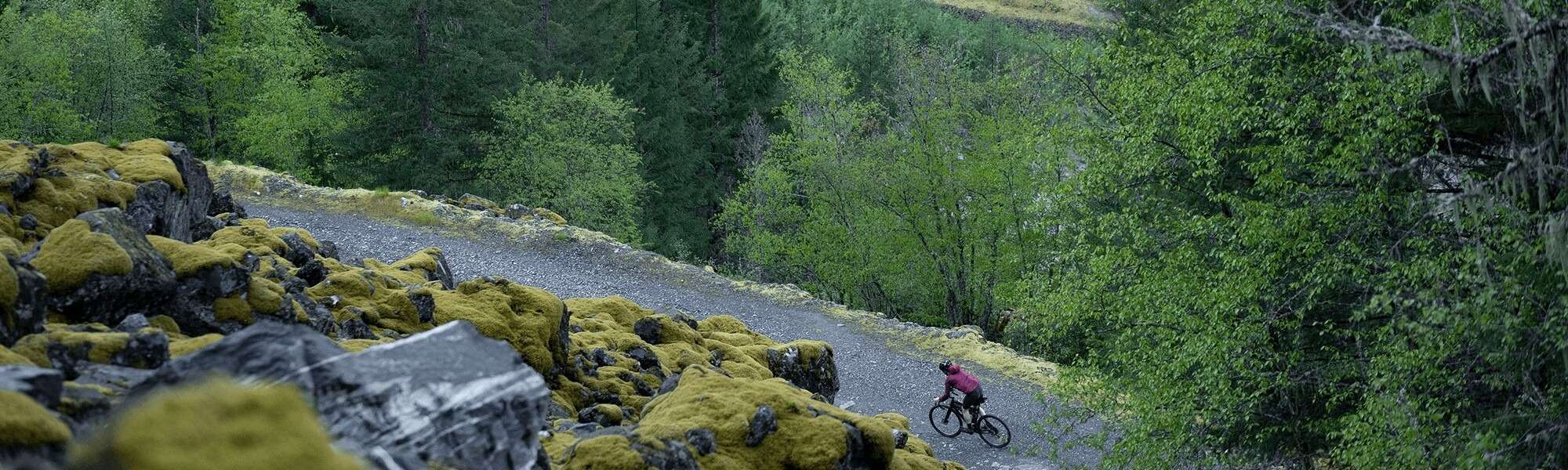 Aerial view of a cyclist riding on a curving gravel road that lines a rocky cliff