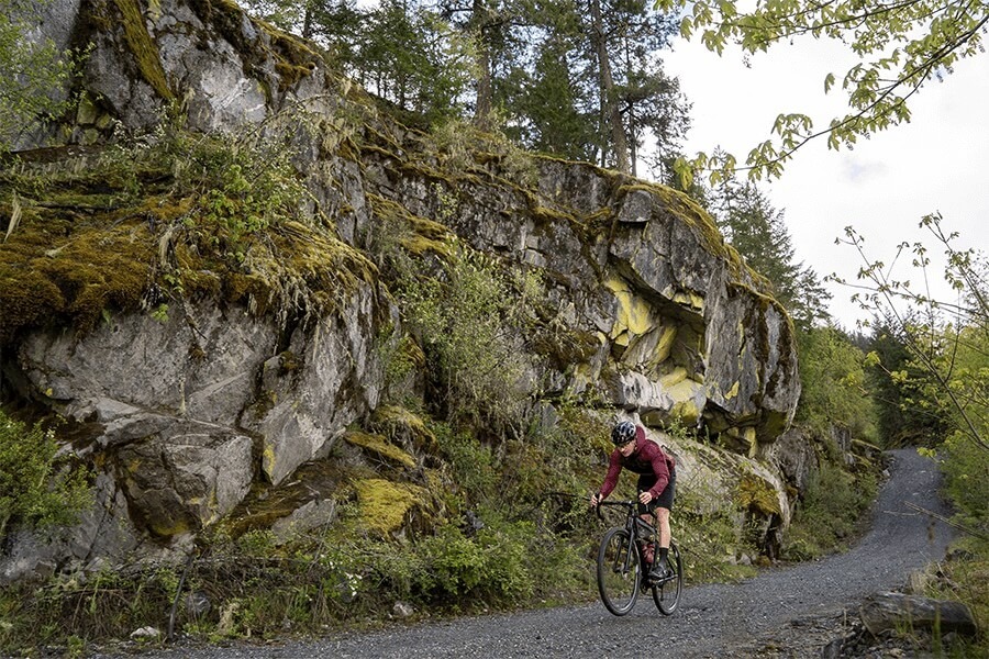 Cyclist rides on a gravel road alongside a jagged rock wall