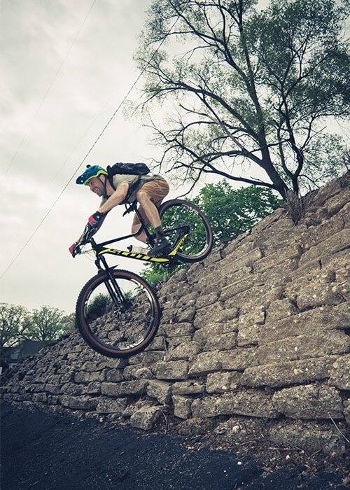 A mountain biker rides his bike off a brick retaining wall