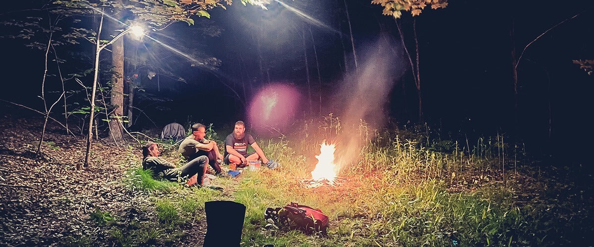 Three cyclist sit together around a campfire at night
