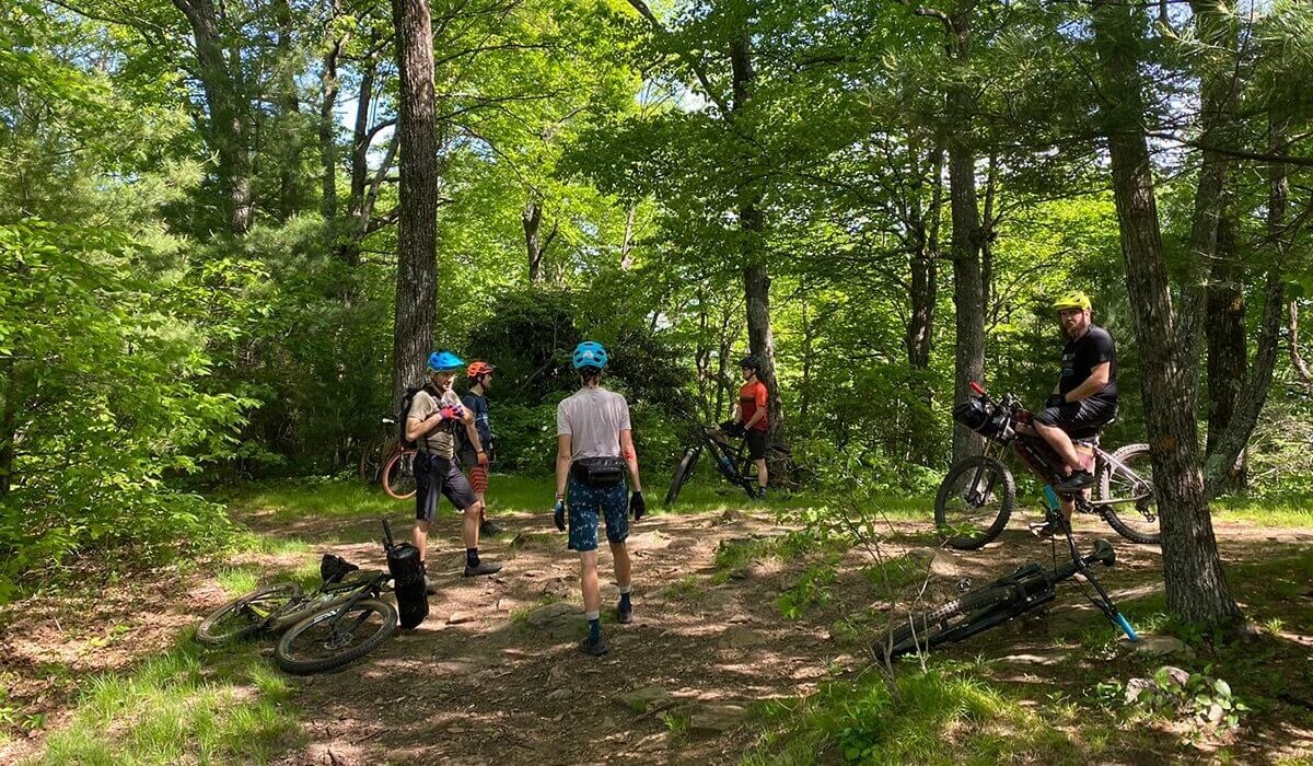 A group of mountain bikers gather around and talk on the trail.