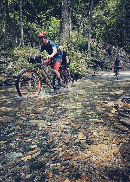 Two cyclists ride their bikes together through a rocky stream