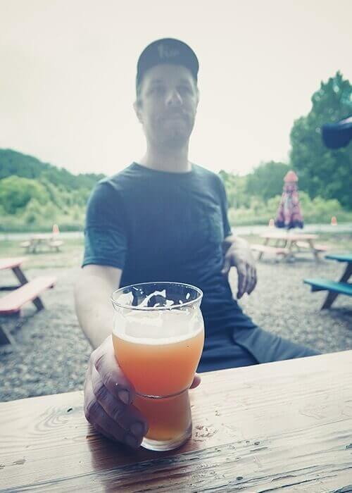 A cyclist sitting at a picnic table holds onto his beer.