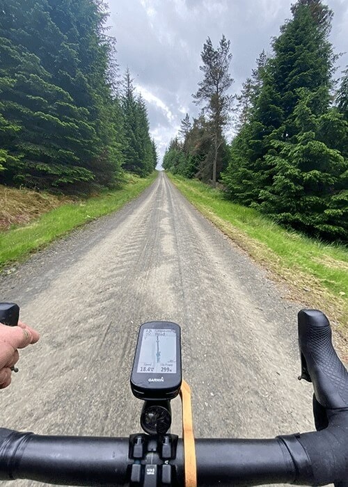 Steve's perspective from above the handlebars. The road ahead is gravel and lined with trees.