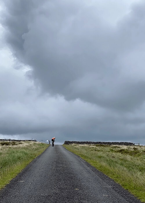 Steve Bate is visible in the distance on a stretch of gravel road with gray skies overhead