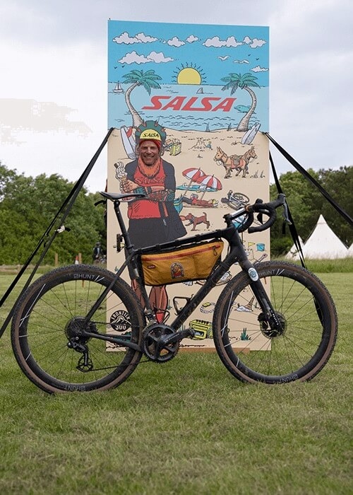 Steve Bate sticks his face into a hole in a Salsa event sign, with his bike in the foreground