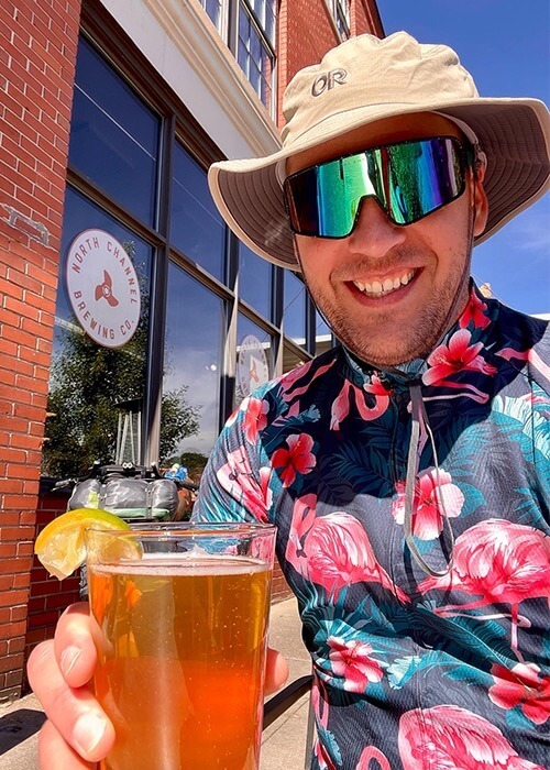 Adam takes a selfie with his beer wearing a cycling jersey and sun hat.