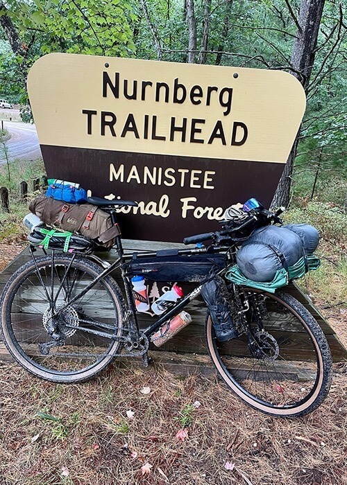 Adam's bike is leaned against the sign for the Nurnberg Trailhead in Manistee National Forest.