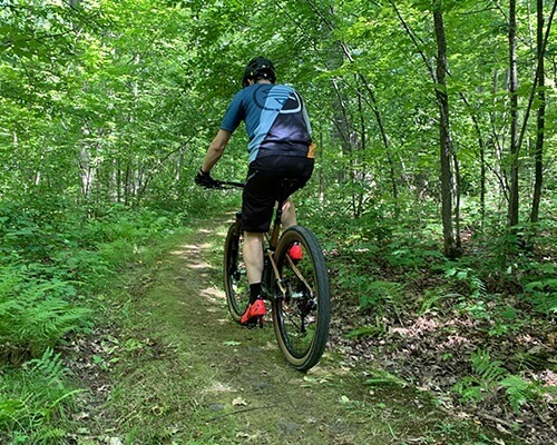 Paul is shown from behind riding on a narrow wooded dirt trail