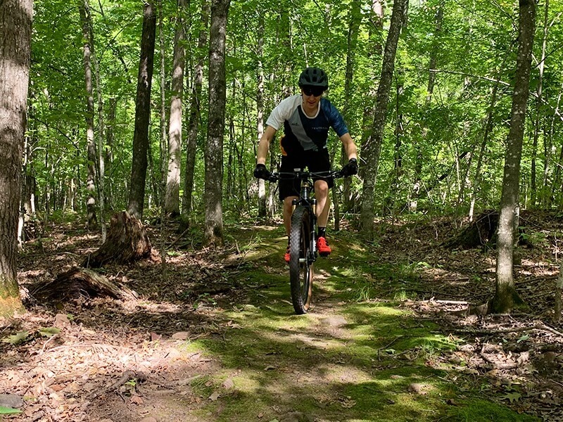 Paul is shown from the front riding his mountain bike on a mossy trail in the woods