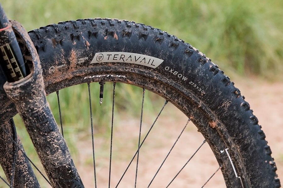 A closeup view of a mountain bike's muddy front wheel, fitted with the Oxbow tire