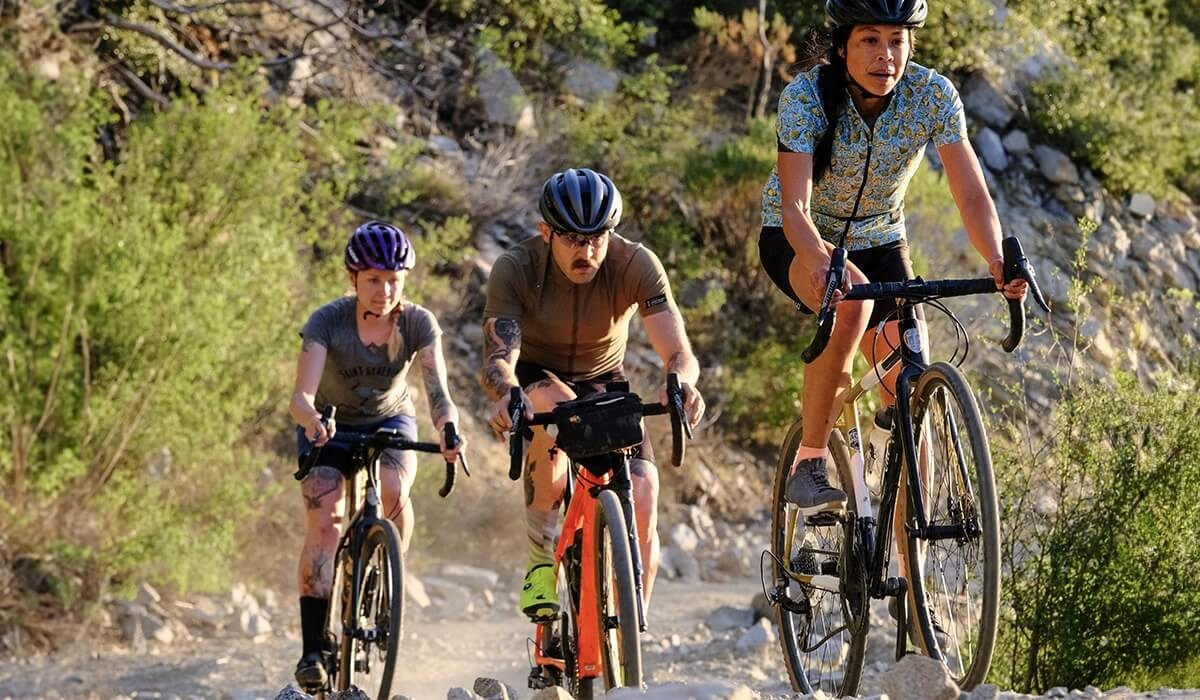 A group of cyclists on gravel bikes ride uphill on rocky terrain.