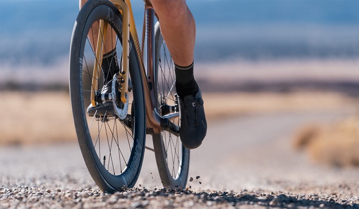 A closeup view of the lower half a road bike on gravel and a cyclist's feet on the pedals