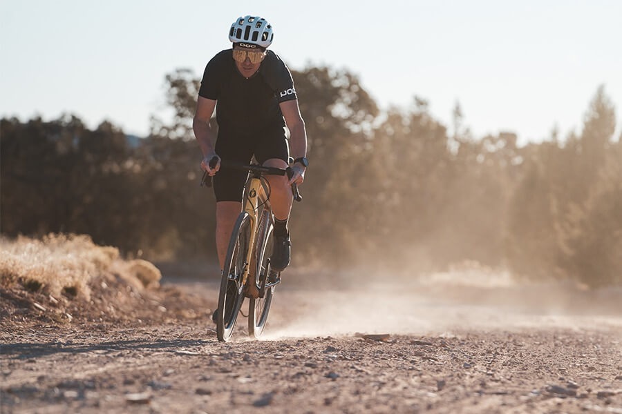 Cyclist on a gravel bike rides on a gravel road with dust trailing behind