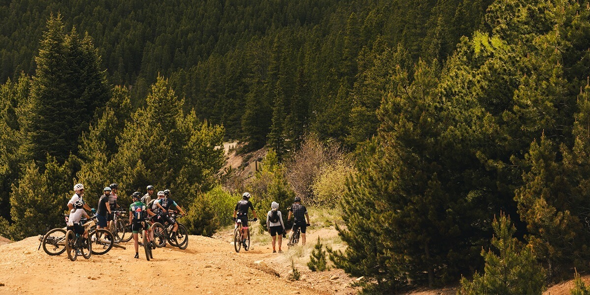 A group of cyclists stand with their bikes while descending down a gravel path on a mountain