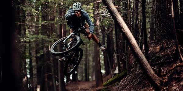 Mountain biker riding in forest catching air off jump doing one-footed table-top