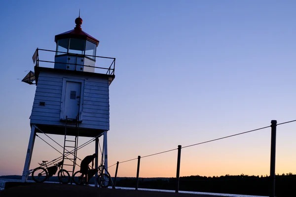 A lighthouse near the water is shown at sunset