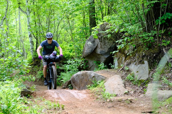 A cyclist rides on a narrow dirt trail on a bike loaded with gear