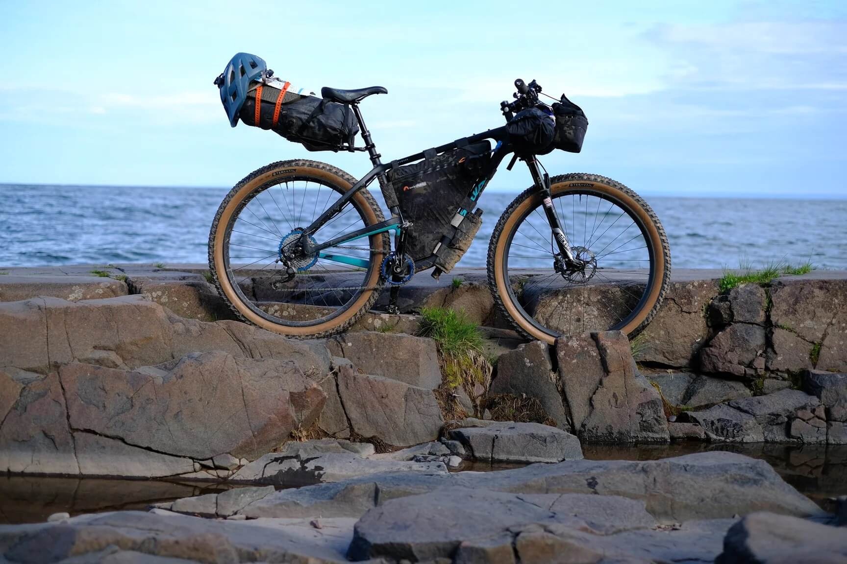 A loaded gravel bike is placed atop rocks along the shore of the lake