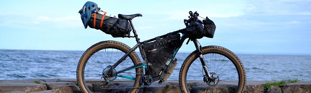A gravel bike sits next to the lake loaded with camping gear