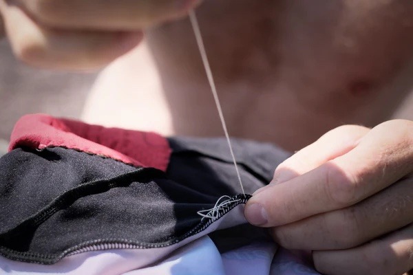 A closeup of needle and thread being used to mend clothing
