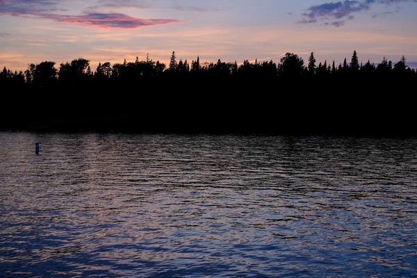 Surface of the lake at dusk with silhouettes of pines in the back