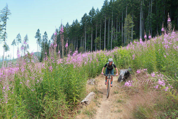 Courtney riding a mountain bike on a dirt trail lined with tall wildflowers