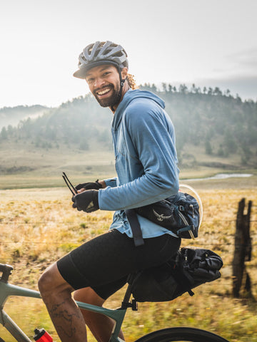 Jalen sitting on his gravel bike wearing riding gear and smiling in front of a mountain range