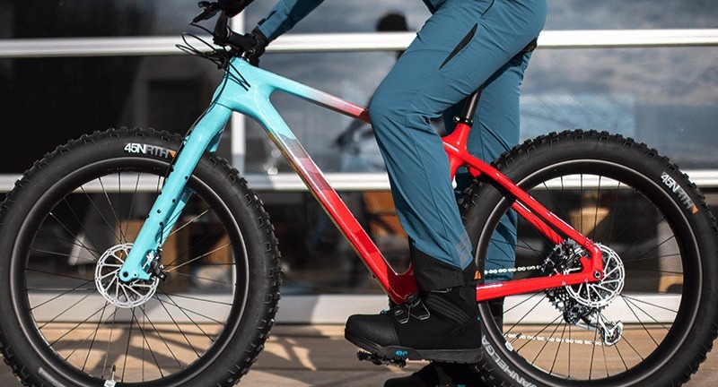 A cyclist stands over a fat tire bike while wearing 45nrth winter cycling pants in the slate colorway.