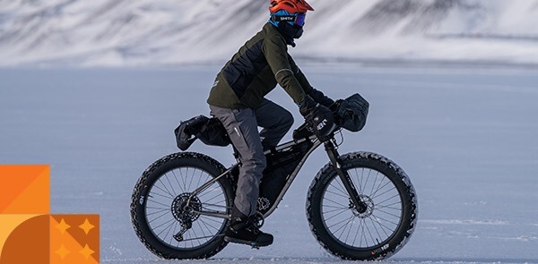 A cyclist rides over a frozen tundra on a fat bike wearing a 45NRTH Naughtvind jacket and pants.