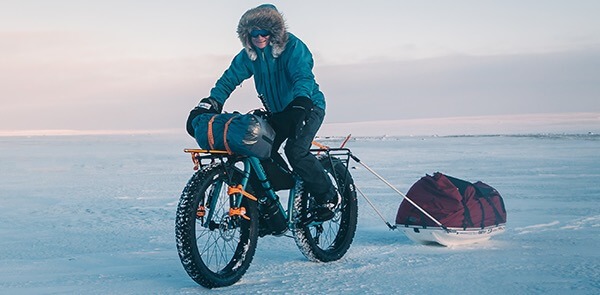 Joffrey rides his fat bike across and icy snowy field whie pulling a sled of gear.