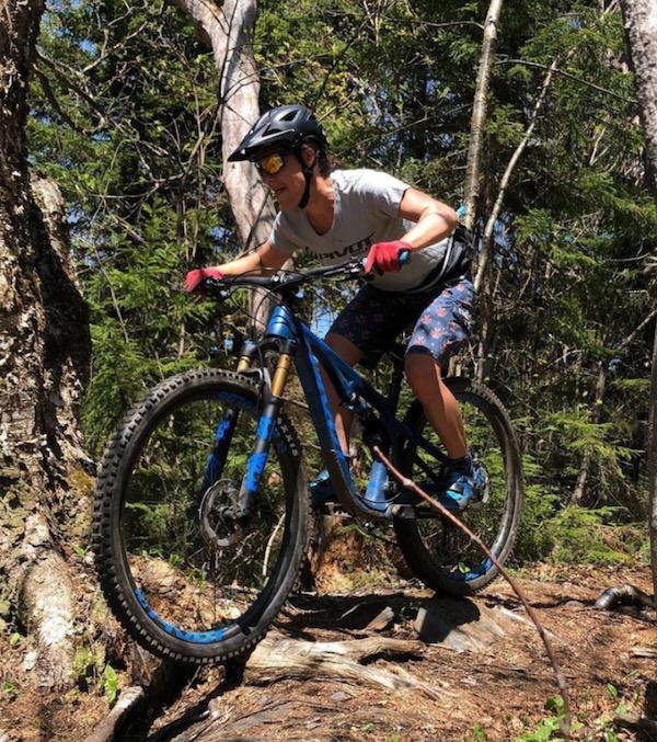 Elisa Otter riding a mountain bike over a tree root on a trail
