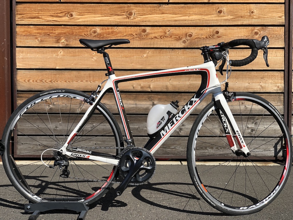A photo of a white carbon EMX-3 Merckx road bike with black and red highlight. It has a Shimano Ultegra groupset. 