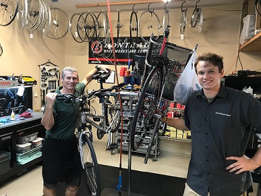 Two of our mechanics smiling and holding a bike.